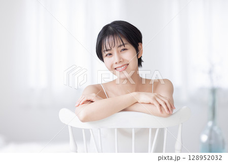 椅子を跨いで座るキャミソールの若い女性 椅子を跨いで座るキャミソールの若い女性 128952032