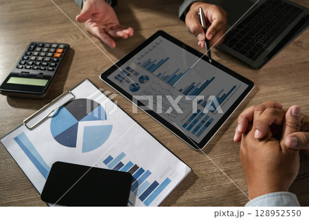 Economics economy Business idea Business meeting discussing data analysis with charts and graphs tablet, surrounded by calculator, laptop 128952550