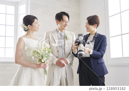 笑顔で会話する新郎新婦とブライダルフォトグラファー 128953182