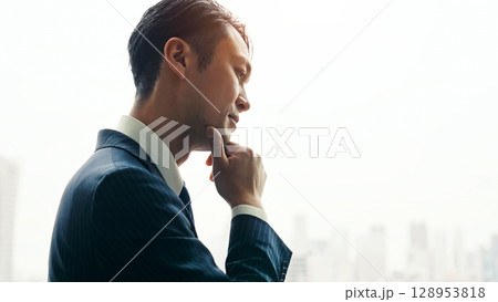 オフィスの窓から都市を眺めながら悩む男性ビジネスパーソン 128953818