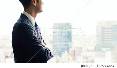 オフィスの窓から都市を眺めながら考えるビジネスマン オフィスの窓から都市を眺めながら考えるビジネスマン 128953823