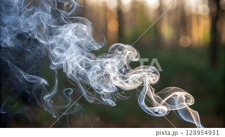 Swirling plumes of white smoke dance against a blurred background of trees, creating an ethereal scene with light and shadow 128954931