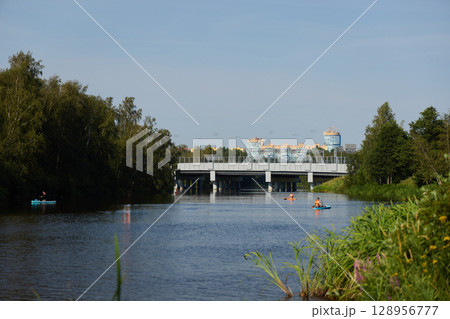 A serene river scene with kayakers near a modern bridge, surrounded by lush vegetation 128956777