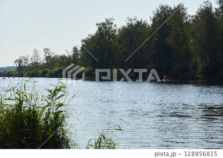A calm river scene shows kayakers navigating lush greenery, evoking tranquility A calm river scene shows kayakers navigating lush greenery, evoking tranquility 128956815