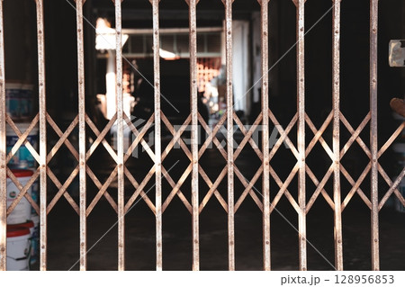 A Closed Shop displaying a Metal Grille Gate against a Dark and Shadowy Background Scene A Closed Shop displaying a Metal Grille Gate against a Dark and Shadowy Background Scene 128956853