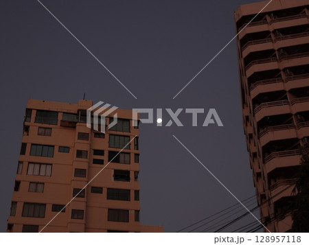A Beautiful Moon Over an Urban Skyline as the Day Turns to Dusk and Night Approaches 128957118