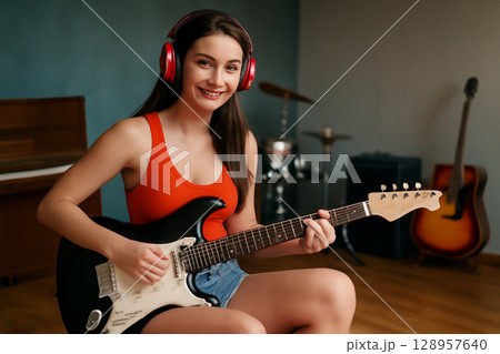 AI generated image of a young woman with a bright smile playing an electric guitar in a music rehearsal studio. She is dressed casually exudes creativity confidence surrounded by musical instruments. AI generated image of a young woman with a bright smile playing an electric guitar in a music rehearsal studio. She is dressed casually exudes creativity confidence surrounded by musical instruments. 128957640