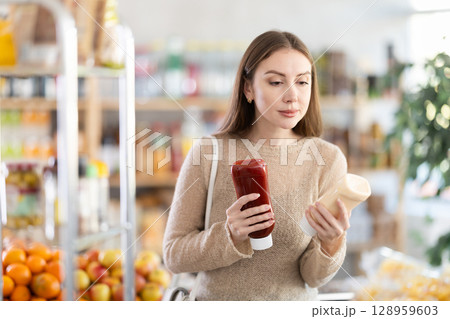 Young woman chooses ketchup or mayonnaise sauces Young woman chooses ketchup or mayonnaise sauces 128959603