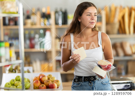 Young femsle shopper selects delicious cheese in supermarket 128959706
