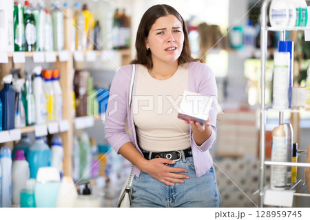 Young woman suffers from abdominal pain, feels pain in her stomach, while visiting household goods supermarket 128959745
