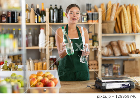 Young woman seller offering water in grocery store 128959746