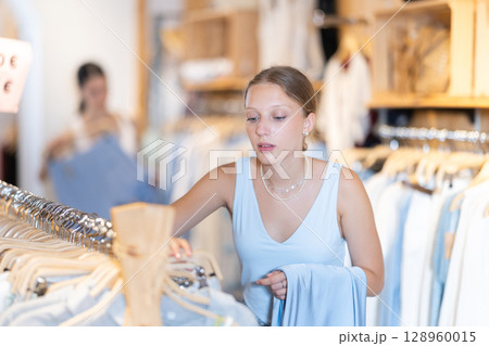 Young woman chooses skirt in clothing store Young woman chooses skirt in clothing store 128960015