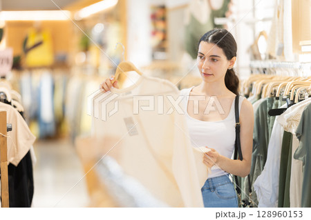 Girl customer chooses blouse in branded store Girl customer chooses blouse in branded store 128960153