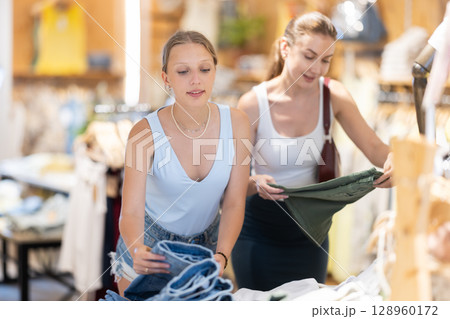 Two girls friends customer chooses denim knee breeches or shorts in store Two girls friends customer chooses denim knee breeches or shorts in store 128960172