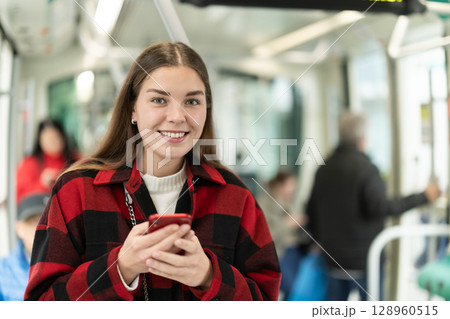 Girl is standing with phone in tram car, getting to work 128960515