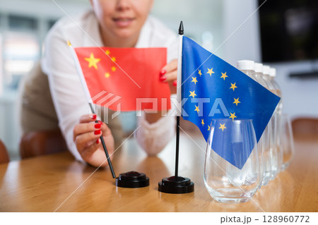 Female secretary places flags of the European Union and China flag on the table before negotiations of top political figures 128960772