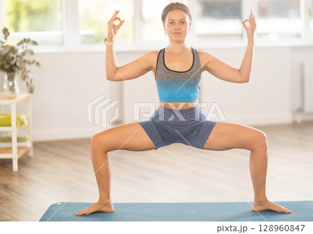 Young woman performing Utkata Konasana with hands in mudra Young woman performing Utkata Konasana with hands in mudra 128960847