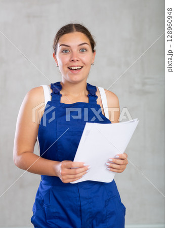 Portrait of emotional woman builder or worker with documents in her hands on gray background Portrait of emotional woman builder or worker with documents in her hands on gray background 128960948