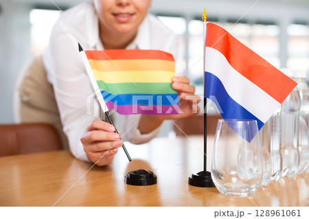 Young woman puts flags of LGBT and Netherlands on table in office 128961061