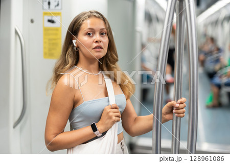 Young woman is standing in subway car with headphones 128961086