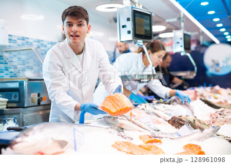 Responsive salesman demonstrating piece of salmon in fish store Responsive salesman demonstrating piece of salmon in fish store 128961098