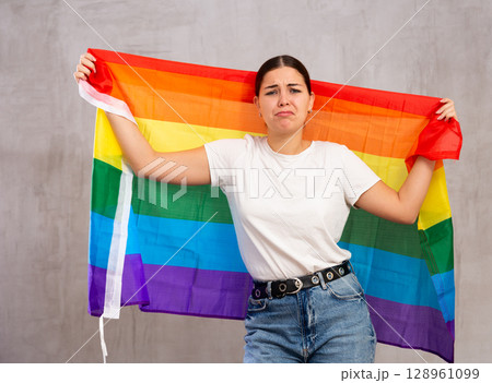 Irritated girl stands with flag of LGBT. Isolated on gray background 128961099
