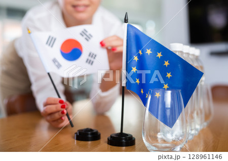 Young woman puts South Korea and EU flags on table in office Young woman puts South Korea and EU flags on table in office 128961146