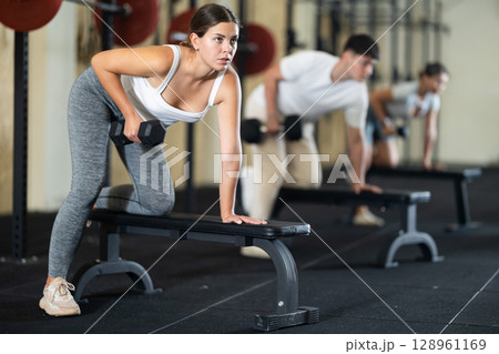 Young woman training with dumbbells on bench Young woman training with dumbbells on bench 128961169