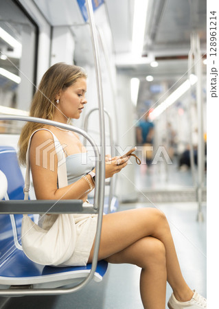 Young woman sitting in subway car with phone Young woman sitting in subway car with phone 128961214