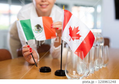 Little flag of Canada on table and flag of Mexico put next to it by young woman Little flag of Canada on table and flag of Mexico put next to it by young woman 128961248
