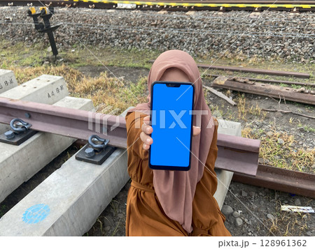 Hijab woman using smart phone with blue screen on railway station Hijab woman using smart phone with blue screen on railway station 128961362