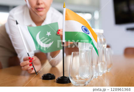 Employee of delegation prepares negotiating table - sets up flag of India and Pakistan 128961368