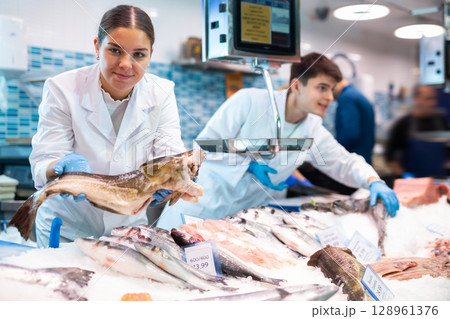 Positive saleswoman holding cod fish in fish store 128961376