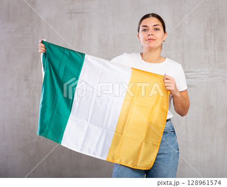 Calm girl stands with flag of Ireland. Isolated on gray background 128961574