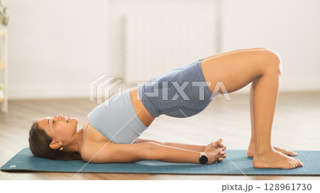 Young girl performing shoulder supported bridge in yoga studio 128961730