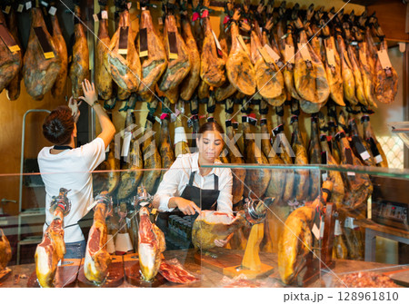 Butcher shop owner and assistant sell Spanish ham 128961810