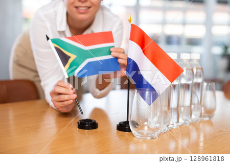 Young woman puts flags of South Africa and Netherlands on table in office 128961818