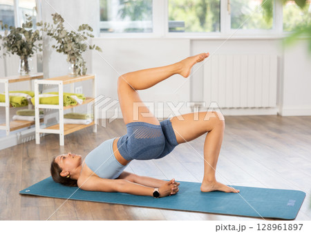 Young woman doing One Legged Bridge Pose in yoga studio 128961897