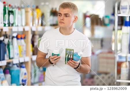 Positive young man choosing toothpaste and toothbrush, dental kit in store 128962009