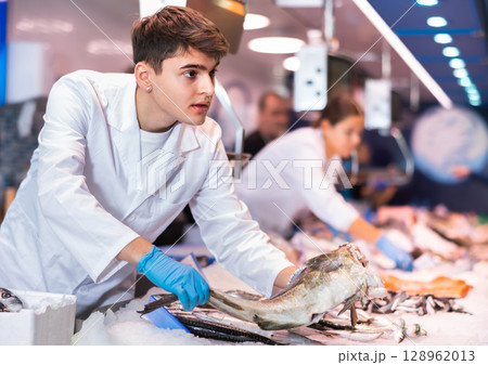 Positive salesman demonstrating cod in fish store 128962013