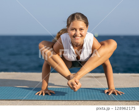 On windy day young slender woman does yoga near sea doing titibasana On windy day young slender woman does yoga near sea doing titibasana 128962175