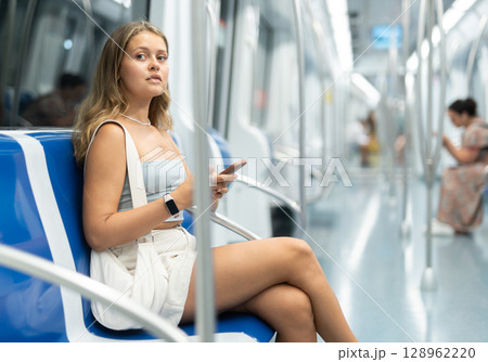 Young woman sitting in subway car with phone Young woman sitting in subway car with phone 128962220