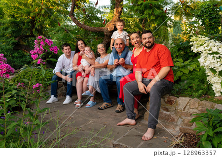 Joyful multi-generation family portrait outdoors in blooming summer garden 128963357