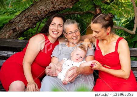 Three generations of women smiling together on park bench Three generations of women smiling together on park bench 128963358