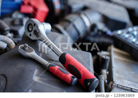 Close-up of wrench socket tool lying on car engine during maintenance work. Vehicle repair concept Close-up of wrench socket tool lying on car engine during maintenance work. Vehicle repair concept 128963869