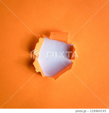 Hole ripped in orange paper on white background. Hole ripped in orange paper on white background. 128964145