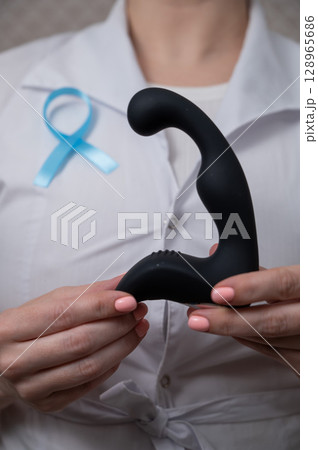 Female doctor holding prostate massager and blue ribbon. Symbol of fight against prostate cancer. Female doctor holding prostate massager and blue ribbon. Symbol of fight against prostate cancer. 128965686