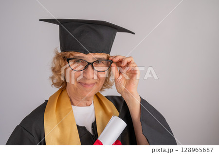 Portrait of an elderly woman in a graduation gown on a white background. Portrait of an elderly woman in a graduation gown on a white background. 128965687