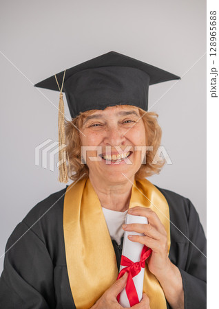 Happy senior woman in graduation gown holding diploma on white background. Happy senior woman in graduation gown holding diploma on white background. 128965688