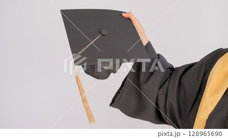 Hand of an elderly woman with a graduation hat on a white background.  128965690